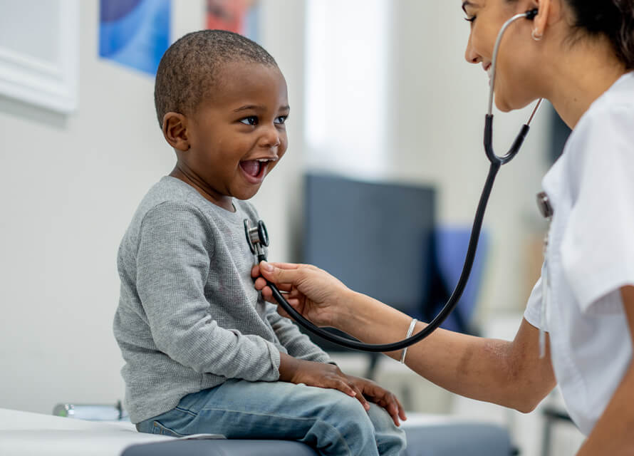 Happy child sitting on hospital table with a nurse holding a stethoscope