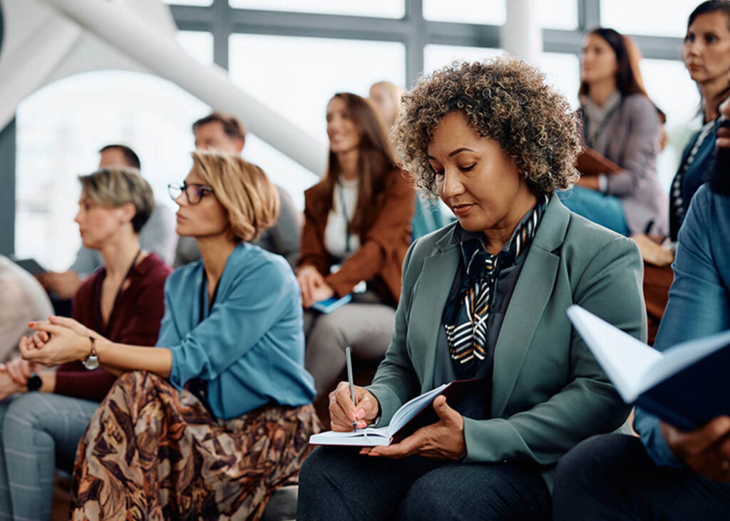 Woman siting in a crowd taking notes inside