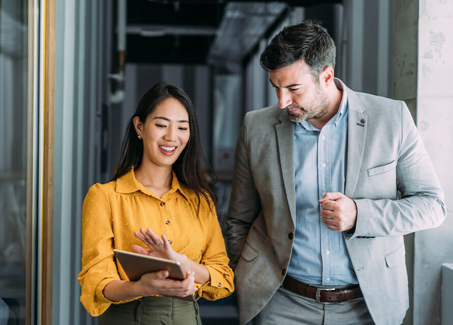 Man and woman coworkers walking in the hallway looking at a tablet