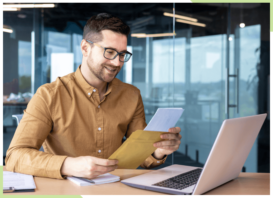 Man opening an envelope sitting in front of laptop