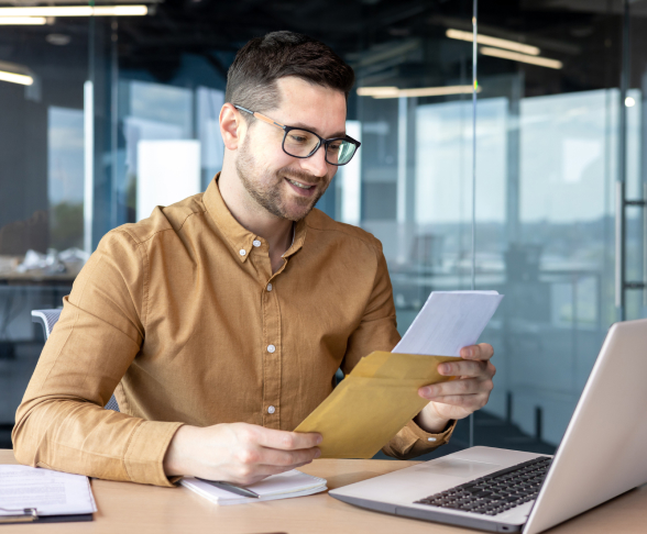 Man opening an envelope sitting in front of laptop