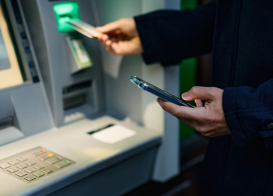 Close up of person using ATM machine and holding phone