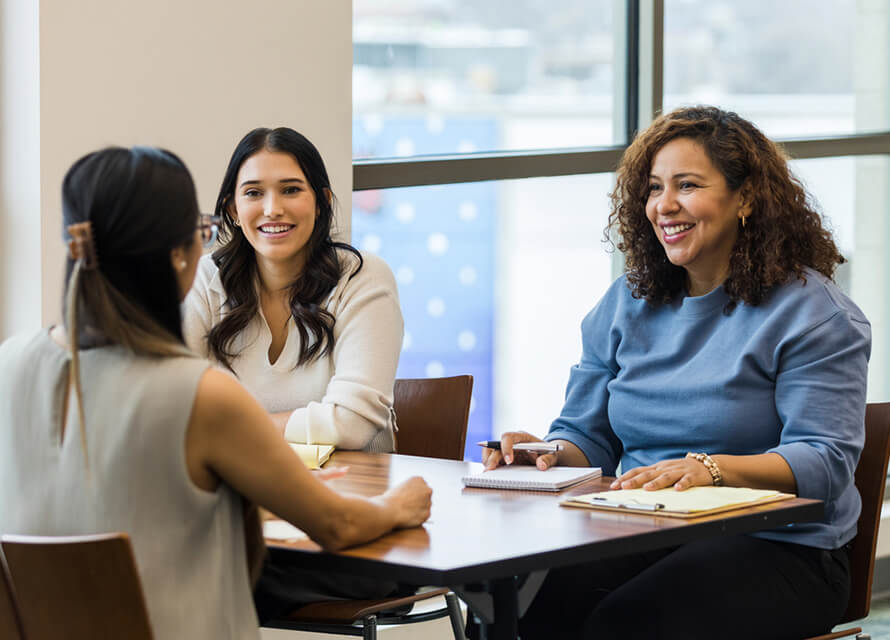 Three women sitting down at a desk in a professional setting