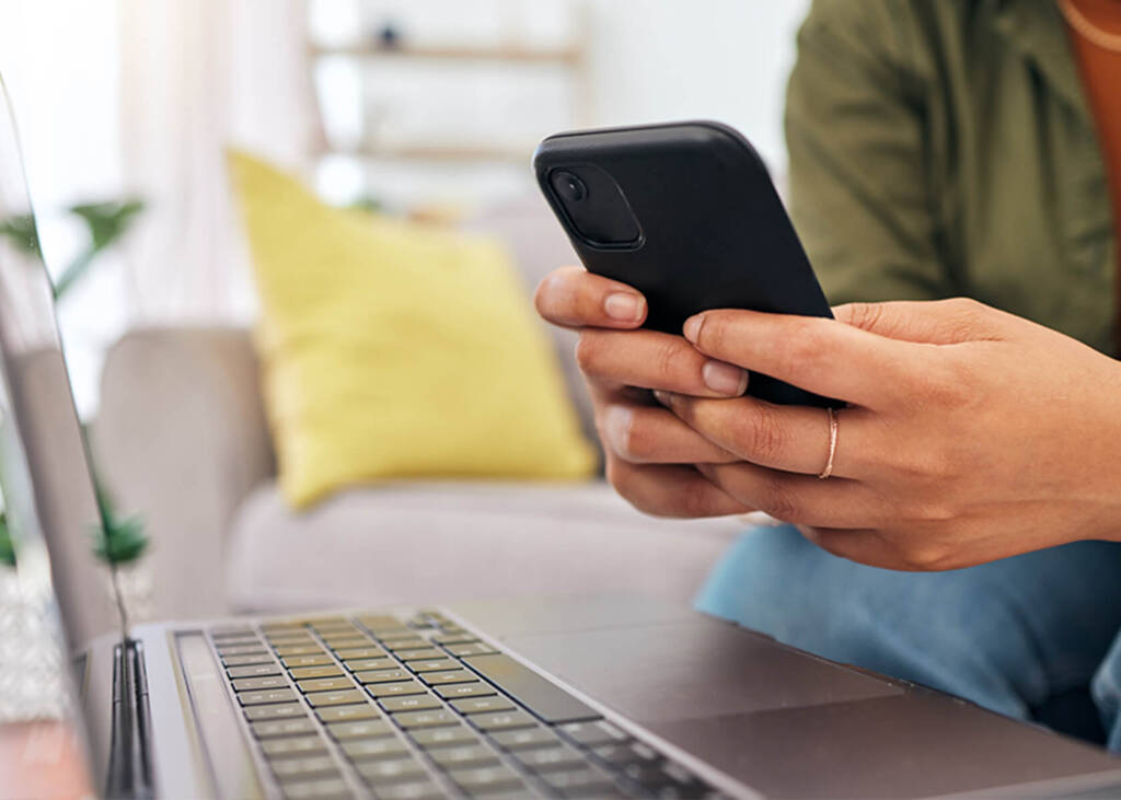 Woman's hands holding phone next to laptop in living area