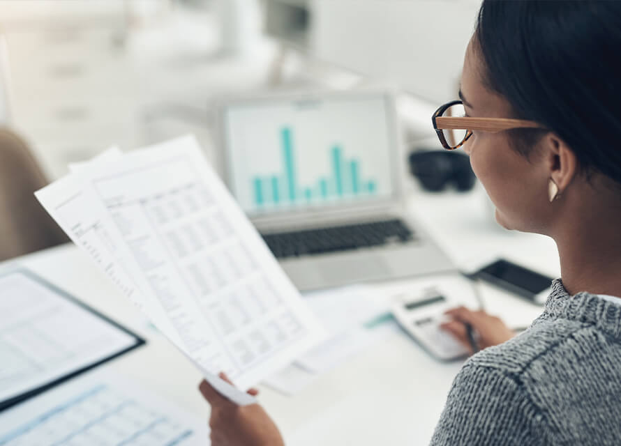 Woman reviewing papers with a calculator and laptop next to her