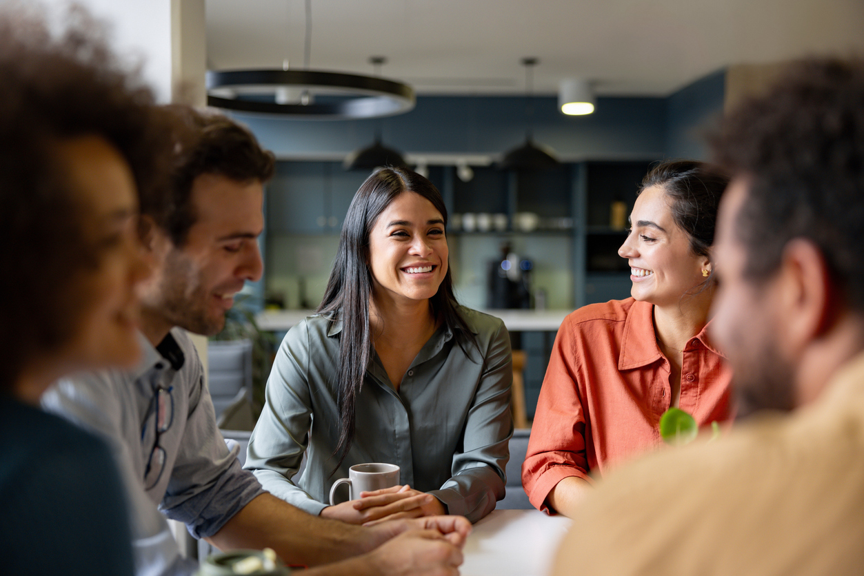 Diverse group of coworkers sitting at a table smiling in the kitchen