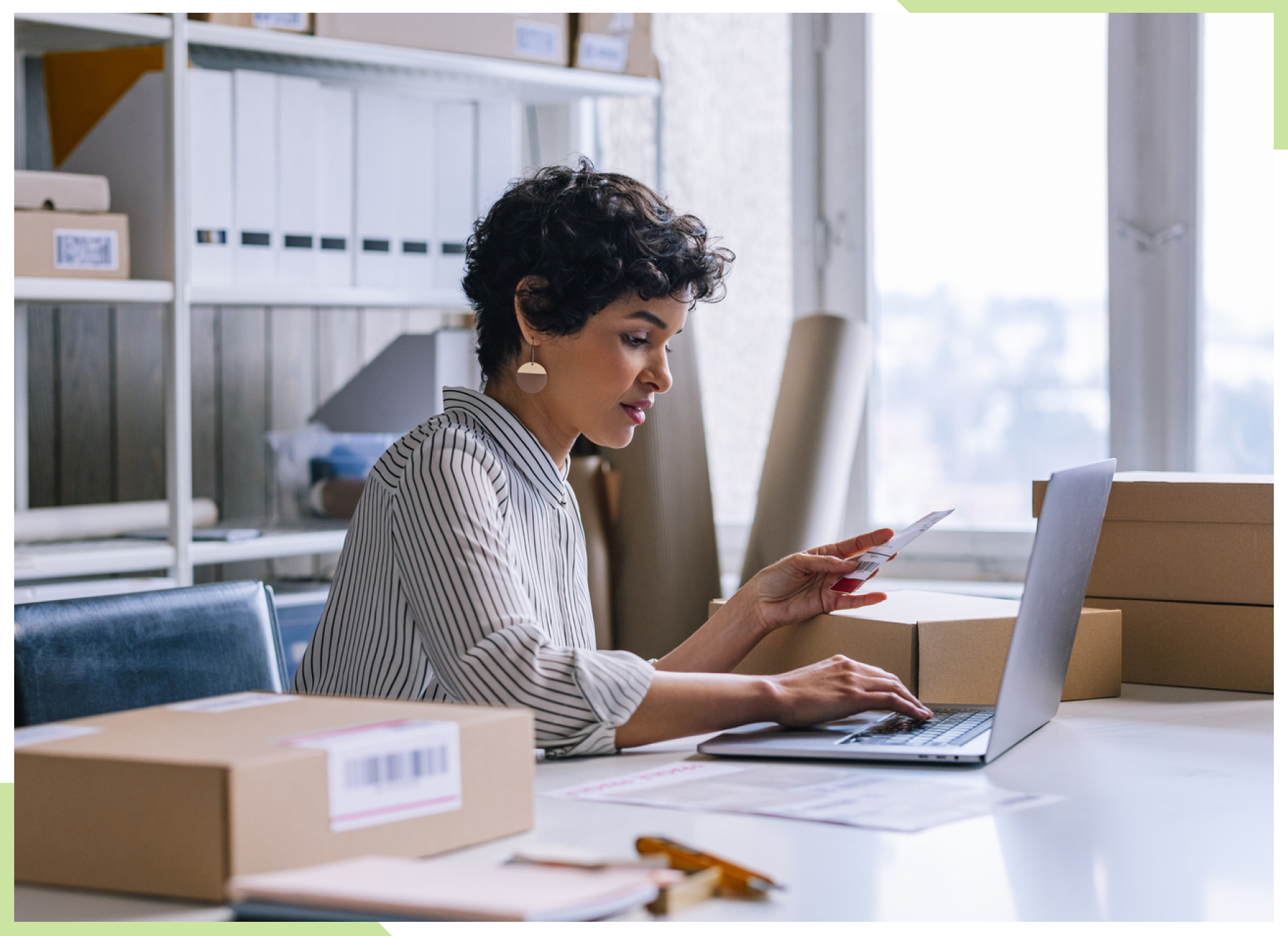 A woman sits at a desk in an office of a small business performing financial transactions at a laptop computer while holding a business invoice. Stock image used for ACH Services